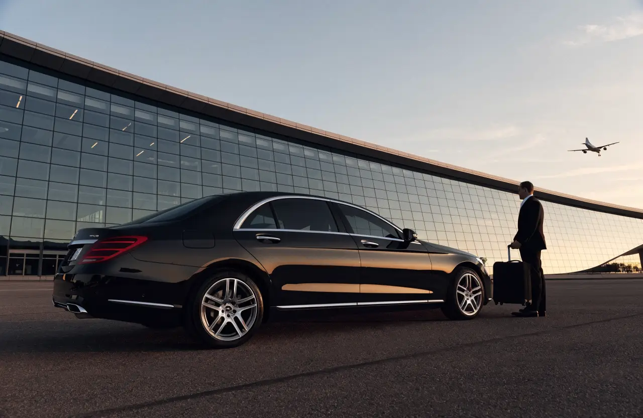 Black luxury sedan and chauffeur at airport arrivals
